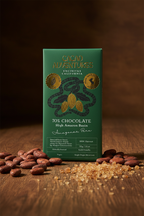 70% Cacao Adventures Dark Chocolate Bar packaging  on a wooden table surrounded by cacao beans and coconut sugar.