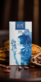 Nomé 73% chocolate bar packaging with blue design on a dark background with cacao pods in the background