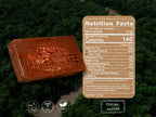 A Ceremonial Cacao Bar embossed with the words 'Cacao Adventure' is shown over an aerial view of a dense green forest. A large brown nutrition facts label is overlaid on the right side, and three small icons at the bottom indicate keto, dairy free, and vegan claims.