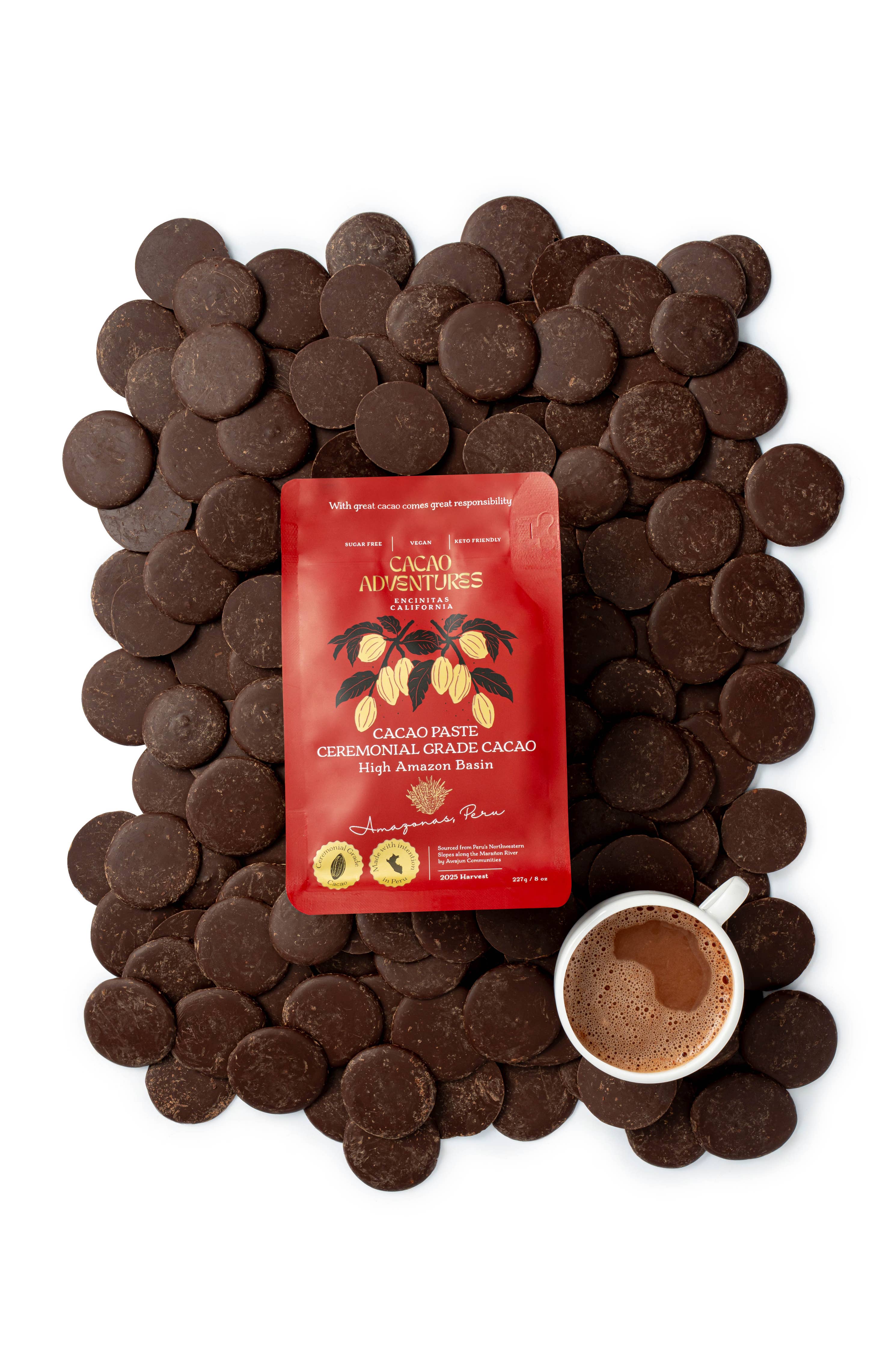 Cacao Adventures Ceremonial Cacao Paste red packaging surrounded by dark cacao paste discs with a cup of prepared ceremonial cacao drink