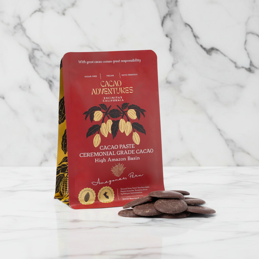 Cacao Adventures Ceremonial Cacao Paste red pouch standing upright with dark cacao paste discs in foreground on marble background, High Amazon Peru