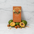 Cacao Adventures 53% Unmilk'd Chocolate with Lucuma bar in orange and gold packaging standing upright on white marble, styled with fresh lucuma fruit and caramel