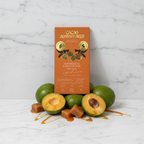 Cacao Adventures 53% Unmilk'd Chocolate with Lucuma bar in orange and gold packaging standing upright on white marble, styled with fresh lucuma fruit and caramel