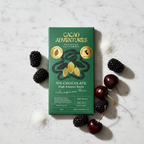 Cacao Adventures 70% High Amazon Basin dark chocolate bar in green and gold packaging standing upright on white marble, styled with raw coconut sugar and dark berries