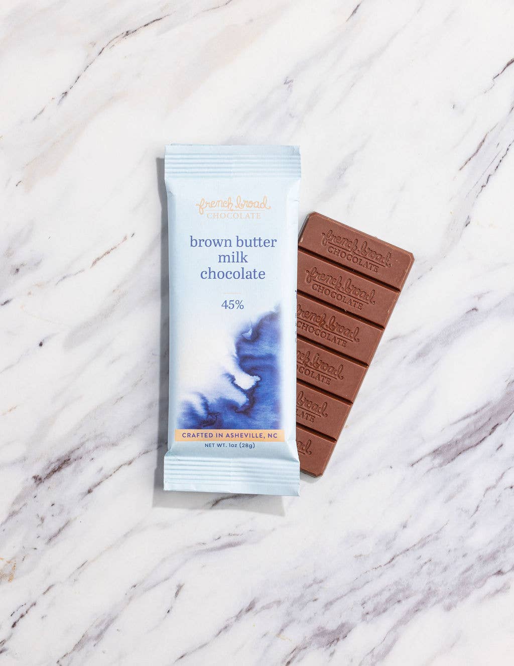 French Broad Chocolate 45% Brown Butter Milk Chocolate bar and light blue packaging on marble surface, crafted in Asheville NC, 1oz 28g