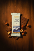 French Broad Chocolate 45% Hazelnut Milk Chocolate light blue packaging standing upright with hazelnuts on wooden surface