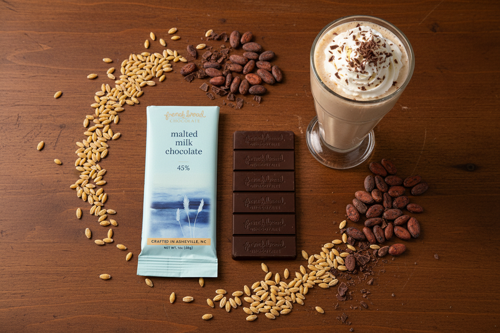 French Broad Chocolate 45% Malted Milk Chocolate bar and packaging flat lay with a milkshake on warm surface, crafted in Asheville NC