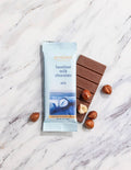 French Broad Chocolate 45% Milk Chocolate Bar with Roasted Hazelnuts and packaging on marble surface, crafted in Asheville NC