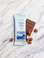 French Broad Chocolate 45% Milk Chocolate Bar with Roasted Hazelnuts and packaging on marble surface, crafted in Asheville NC
