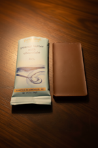 French Broad Chocolate 45% Peanut Butter Milk Chocolate back of bar showing embossed French Broad Chocolate branding next to packaging on dark wooden surface