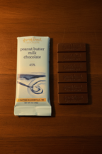 French Broad Chocolate 45% Peanut Butter Milk Chocolate packaging and bar side by side on warm wooden surface showing front label and embossed bar