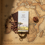 French Broad Chocolate 70% Uganda Dark Chocolate bar in white and gold packaging resting on a vintage illustrated map of Uganda with cacao beans, dried fig, and compass