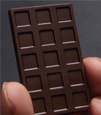 Close-up of an unwrapped chocolate bar held between two fingers, showing its individual square sections.