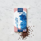 Nomé 93% Chocolate Oscuro bar with Sea Salt and Cacao Nibs on white marble, salmon pink packaging with blue botanical illustration, single-origin Panama, vegan, 70g
