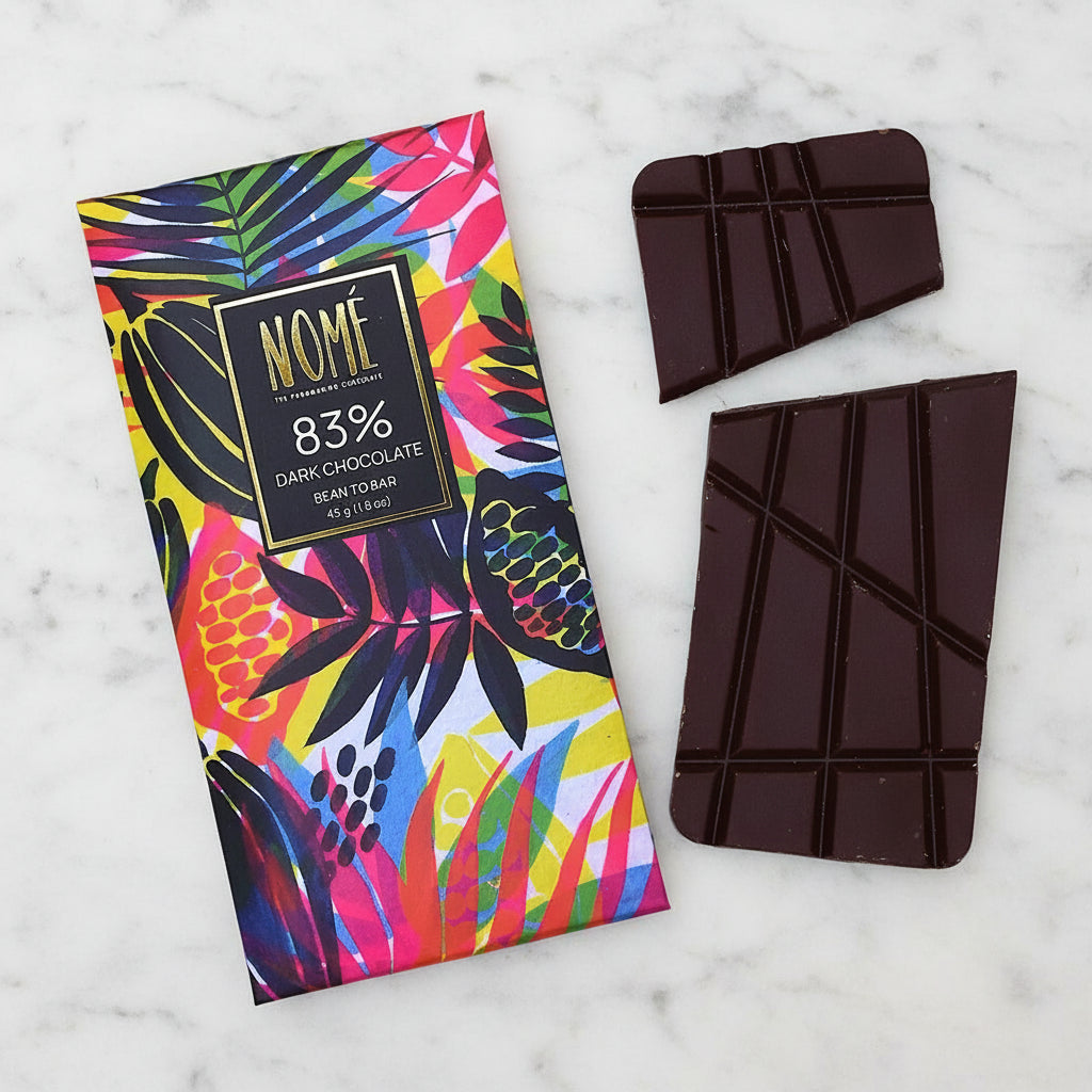 Nomé 83% Dark Chocolate bar unwrapped with vivid tropical print packaging on a marble surface, single-origin Panama, vegan dairy-free