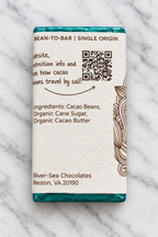 The backside of the 72% Haiti Dark Chocolate Bar from River Sea Chocolates, showing ingredients and a QR Code, on a white marble background.