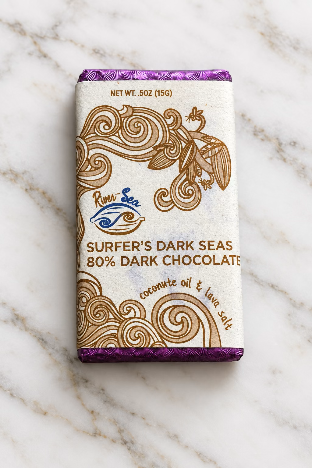 The 80% Surfer's Dark Seas Mini Dark Chocolate bar front packaging from River Sea Chocolates, showing the inclusion of coconut oil and lava salt in the bar, on a white marble background.