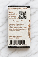 Image of the River Sea Chocolates Cherry Blossom Dark Chocolate mini packaging backside, with a QR Code and ingredients listed on a white marble background.