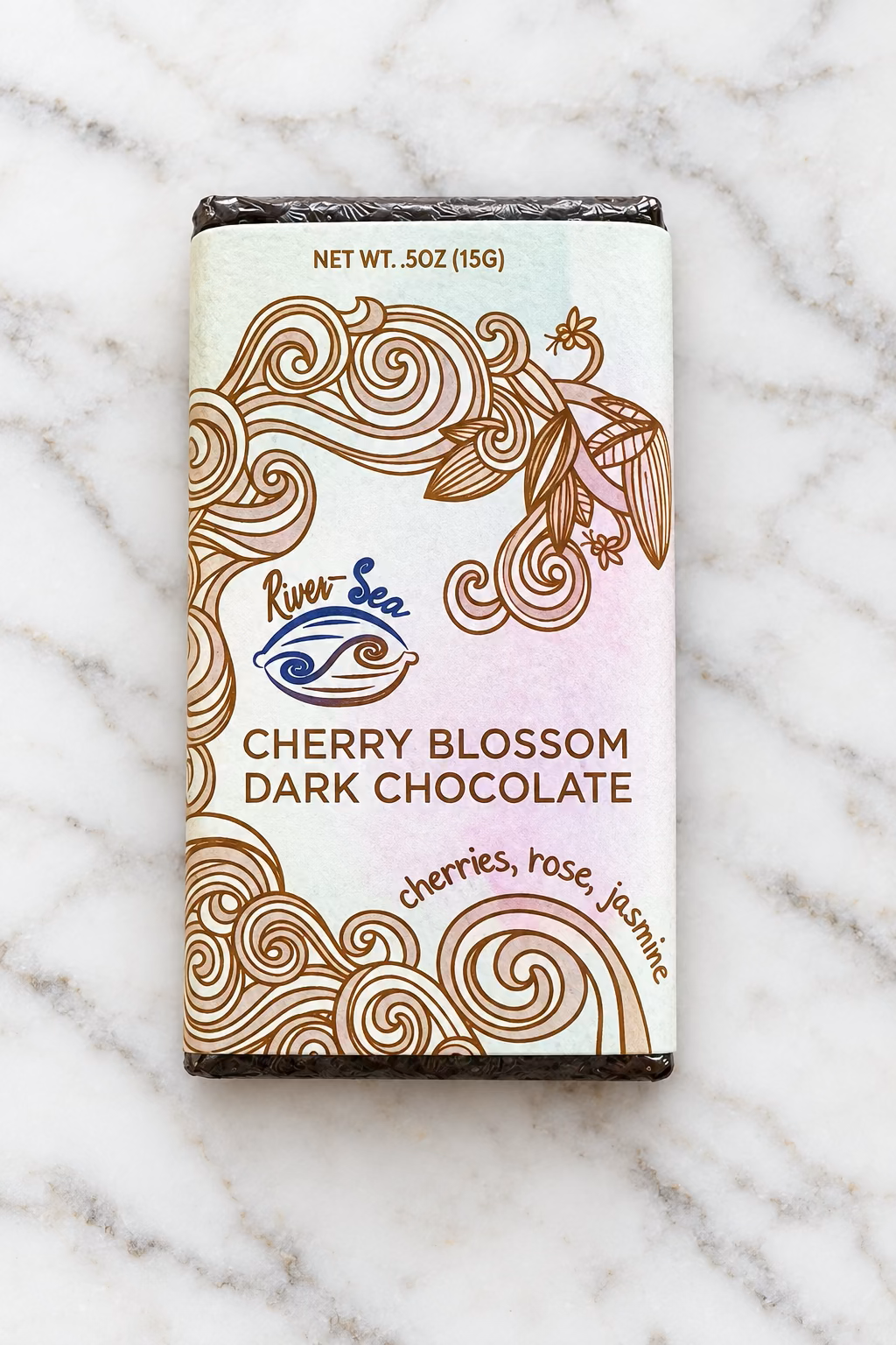 Shot of the River Sea Chocolates Cherry Blossom Dark Chocolate Mini Bar, showing the front packaging on a white marble background.