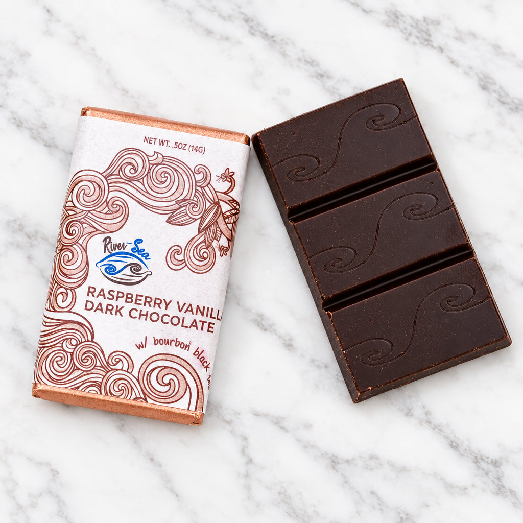 The Raspberry Vanilla Dark Chocolate mini bar from River Sea Chocolate, showing the front of packing and unwrapped bar, on a white marble background.