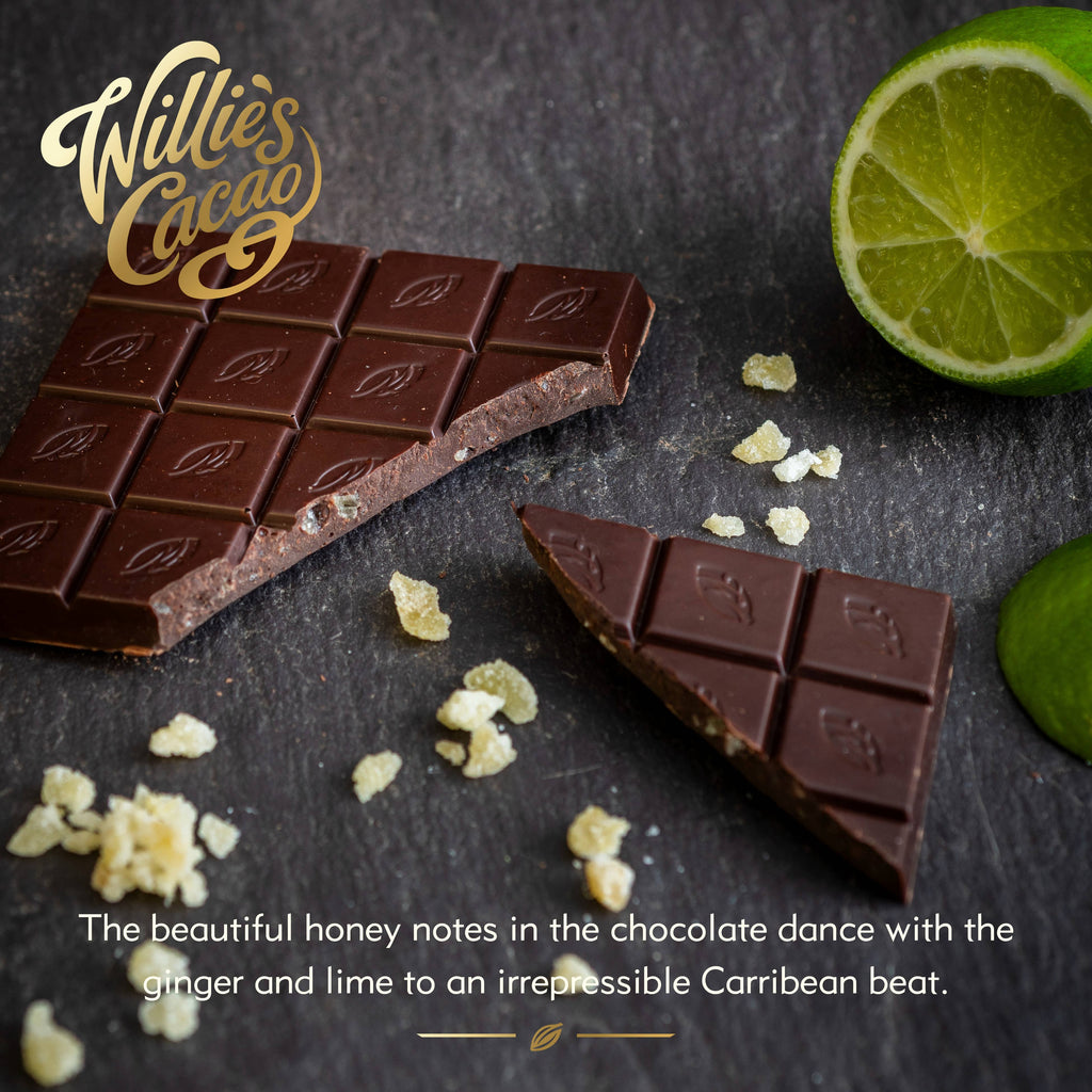 Willie's Cacao Ginger Lime 70% Dark Chocolate bar broken open with crystallized ginger pieces and fresh lime on dark slate surface