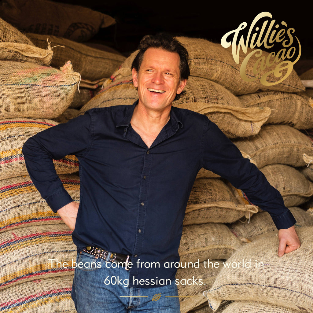 Willie Harcourt-Cooze founder of Willie's Cacao standing in front of stacked 60kg hessian sacks of single estate cacao beans from around the world.