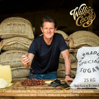 Willie Harcourt-Cooze founder of Willie's Cacao with cacao beans, cocoa butter, and chocolate bars in front of hessian sacks, craft bean-to-bar chocolate maker