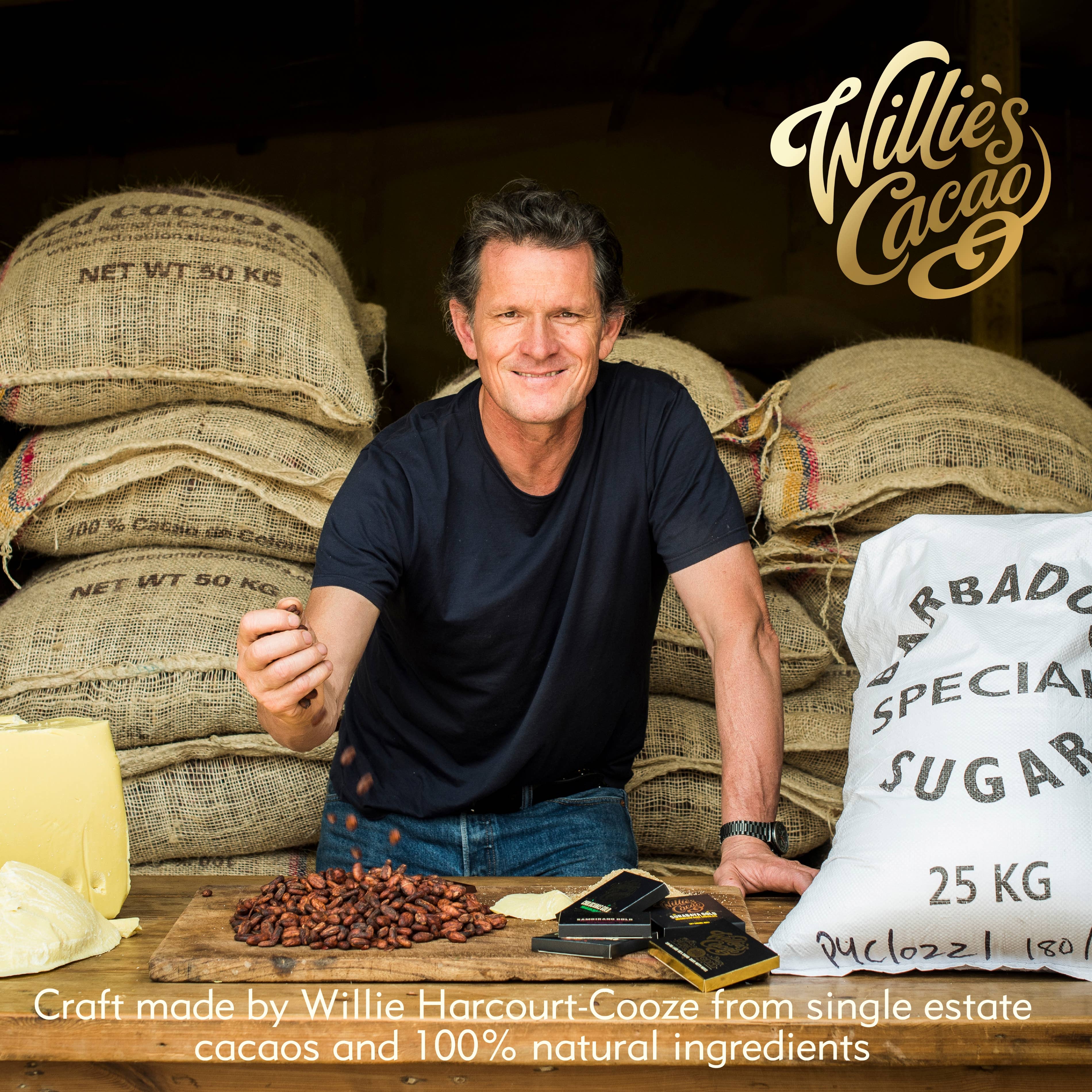 Willie Harcourt-Cooze founder of Willie's Cacao with cacao beans, cocoa butter, and chocolate bars in front of hessian sacks, craft bean-to-bar chocolate maker