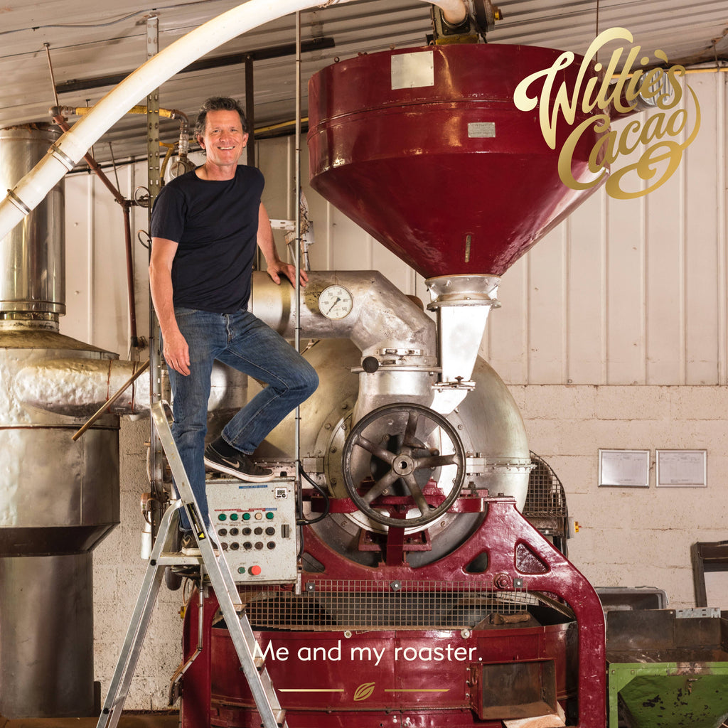 Willie Harcourt-Cooze founder of Willie's Cacao standing on ladder next to large red cacao roasting machine in the Willie's Cacao factory