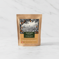Cacao Adventures Ceremonial Grade Cacao Paste kraft pouch on white marble surface, single-origin Piura Peru, sugar-free and vegan