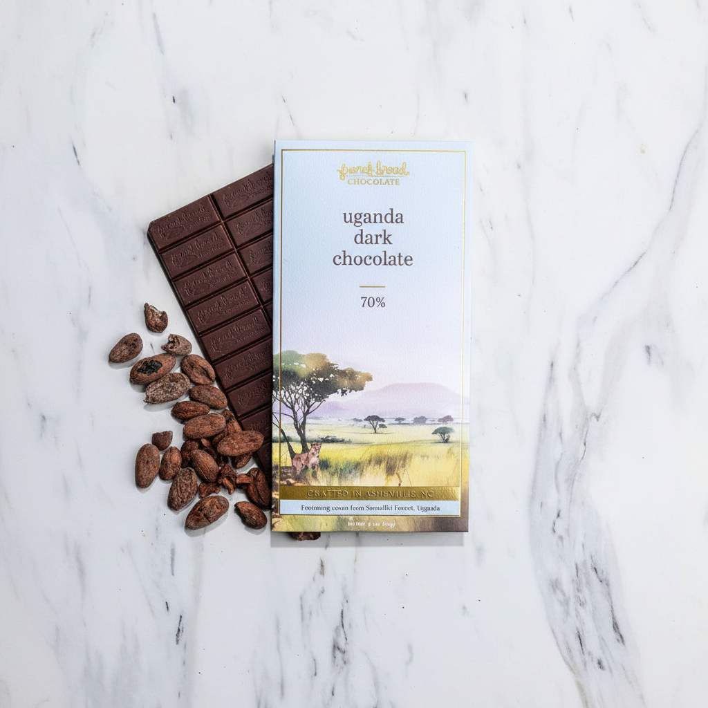 French Broad Chocolate Uganda Dark Chocolate 70% light blue packaging on white marble surface, single-origin Semuliki Forest Uganda, crafted in Asheville NC, 60g