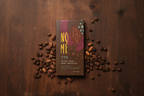 Nomé 77% Geisha Coffee Dark Chocolate bar with roasted Geisha coffee beans on a warm dark wood surface