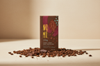 Nomé 77% Geisha Honey Process Dark Chocolate bar surrounded by roasted Geisha coffee beans on a warm cream surface