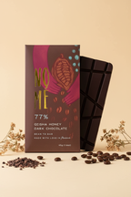Nomé 77% Geisha Honey Dark Chocolate bar with packaging, styled with cacao nibs and dried coffee beans